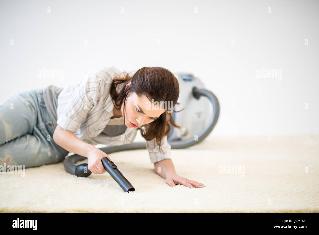 Angry young woman lying on beige carpet and vacuuming it Stock Photo ...