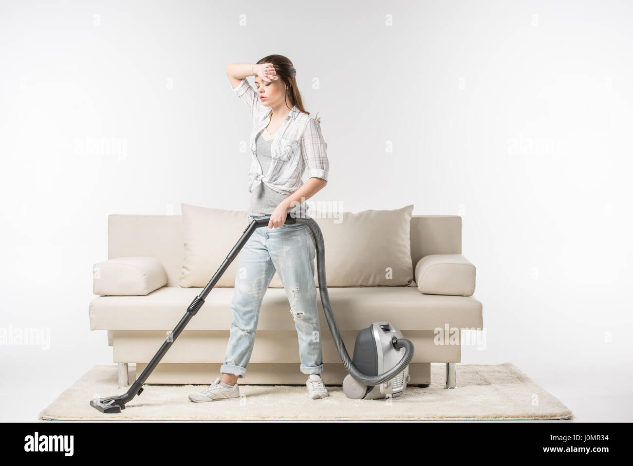 Tired young woman cleaning the carpet with vacuum cleaner Stock Photo ...