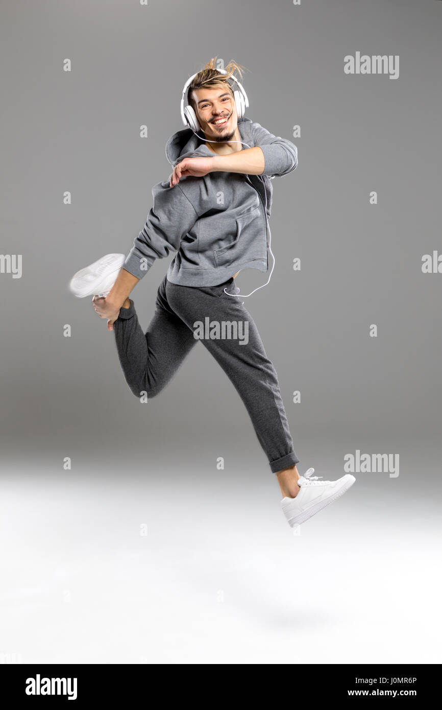 Young athletic man in headphones jumping while smiling at camera Stock Photo