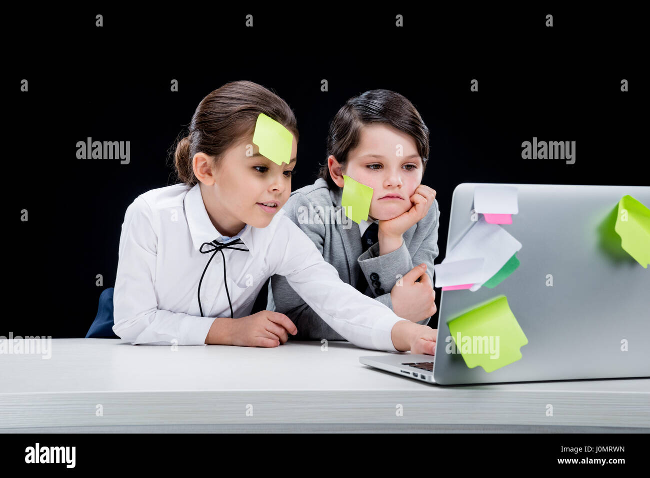 Upset Notes portrait of upset boy and focused girl with notes on faces using laptop ...