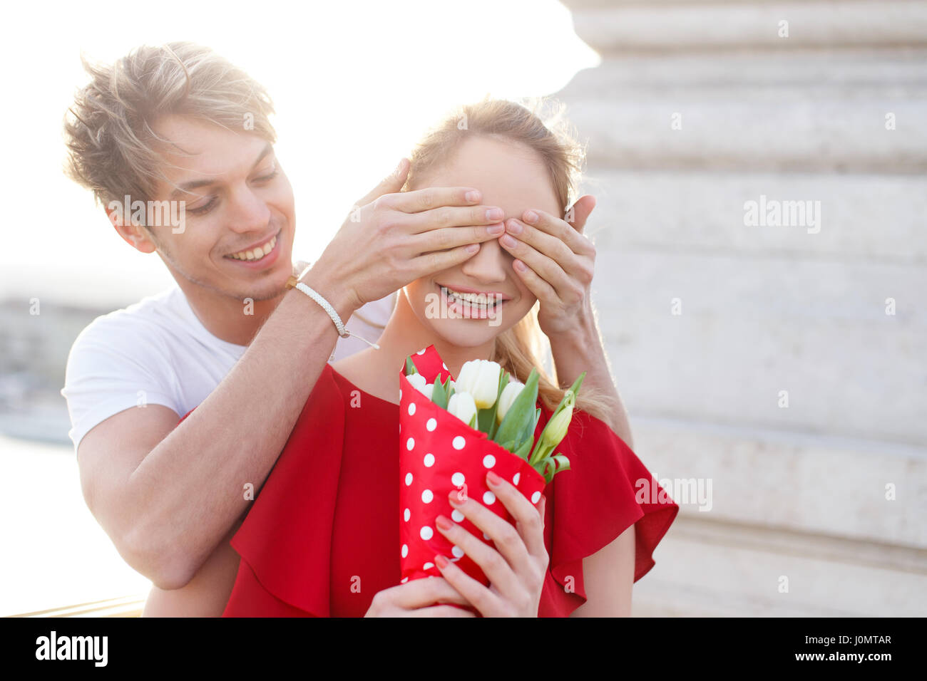 Young blonde woman surprised by man with bouquet, outdoor Stock Photo