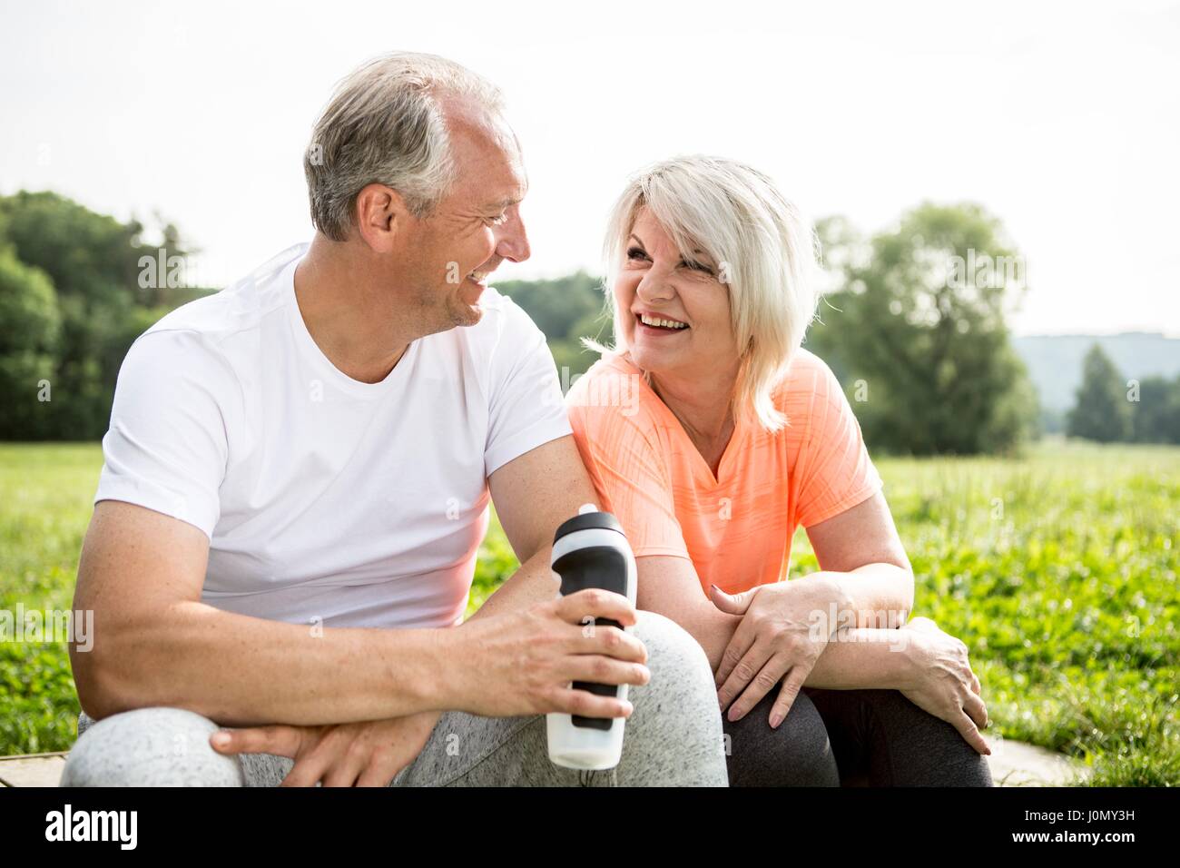 Mature couple sitting outdoors resting, man holding water bottle. Stock Photo