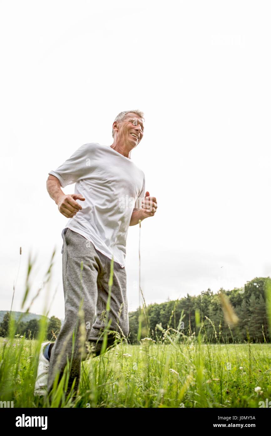 Senior man jogging in grass. Stock Photo