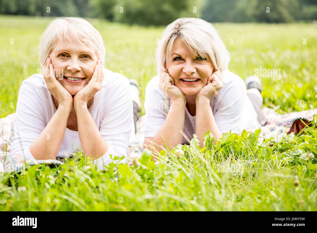 Two women lying on grass with hands on chin. Stock Photo