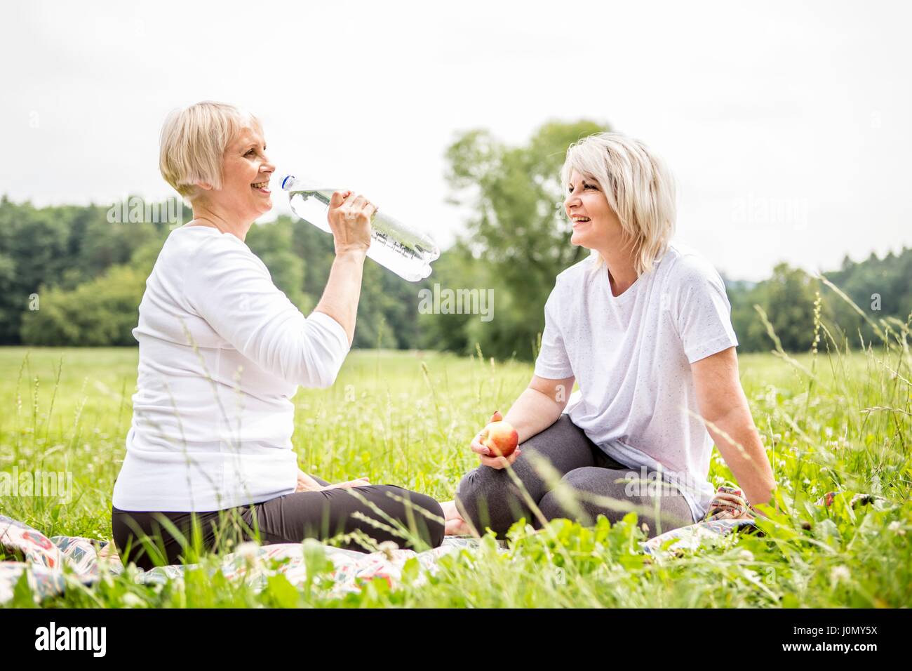 Two women sitting on grass, one drinking water. Stock Photo