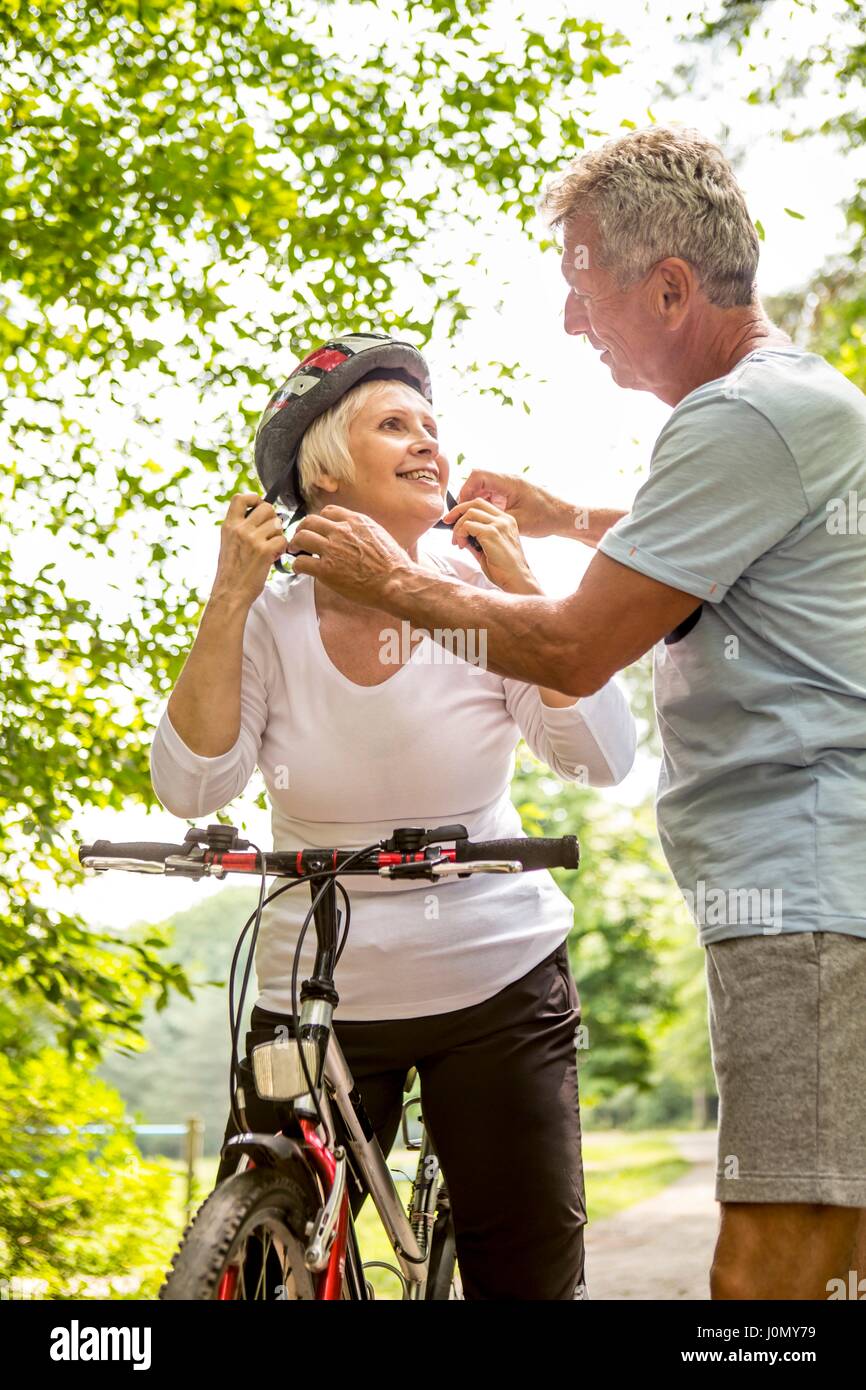 Mature woman on bike, senior man assisting with helmet. Stock Photo