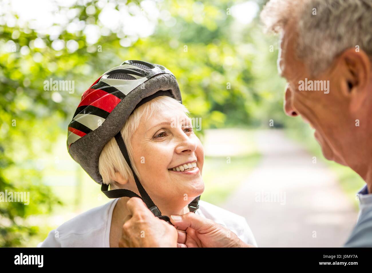 Mature woman wearing bicycle helmet, senior man assisting. Stock Photo