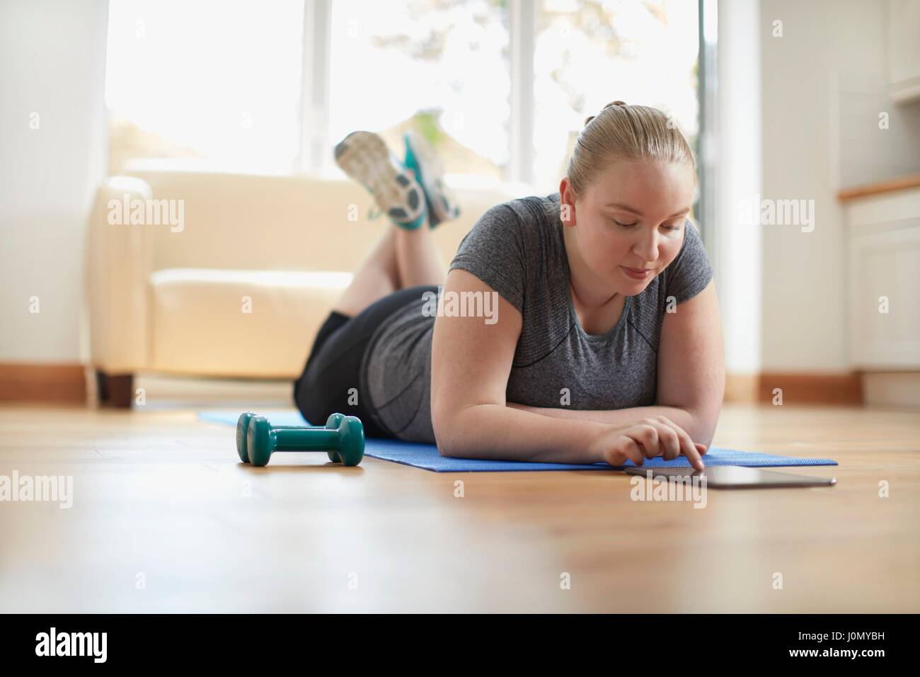 Young woman lying on yoga mat using digital tablet. Stock Photo