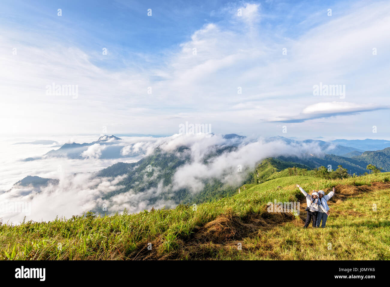 Two female tourists, mother and daughter stand waving amidst the beautiful natural landscape of mountain range sky cloud and fog in the winter Stock Photo