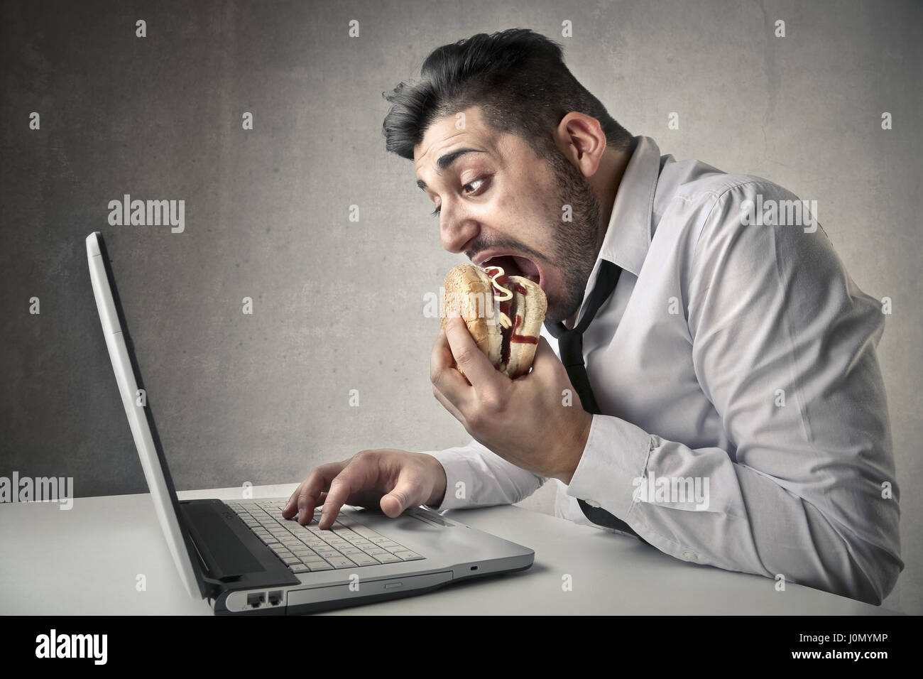 Man eating hamburger while looking at laptop Stock Photo