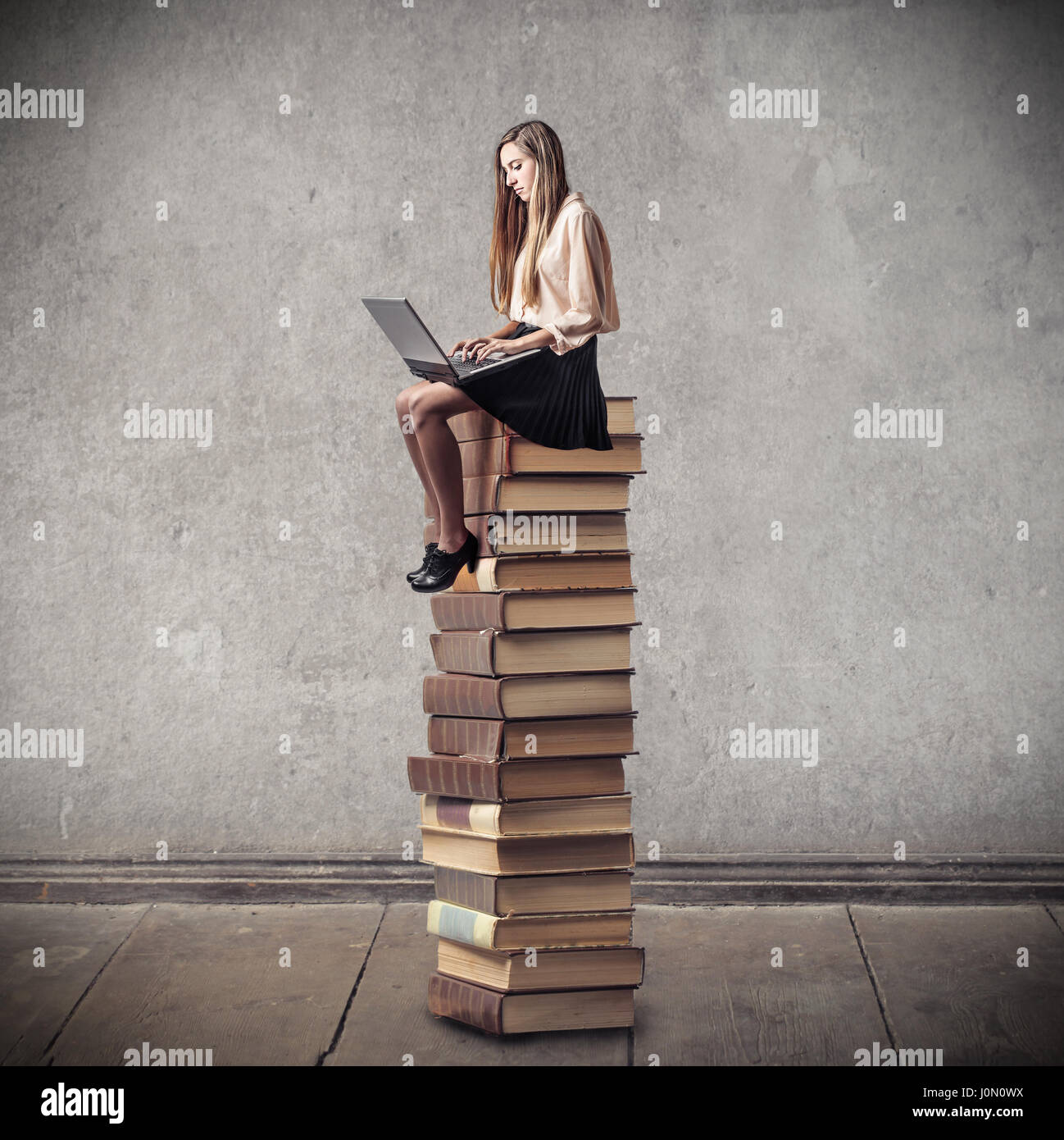 Young woman sitting on pile of books Stock Photo - Alamy