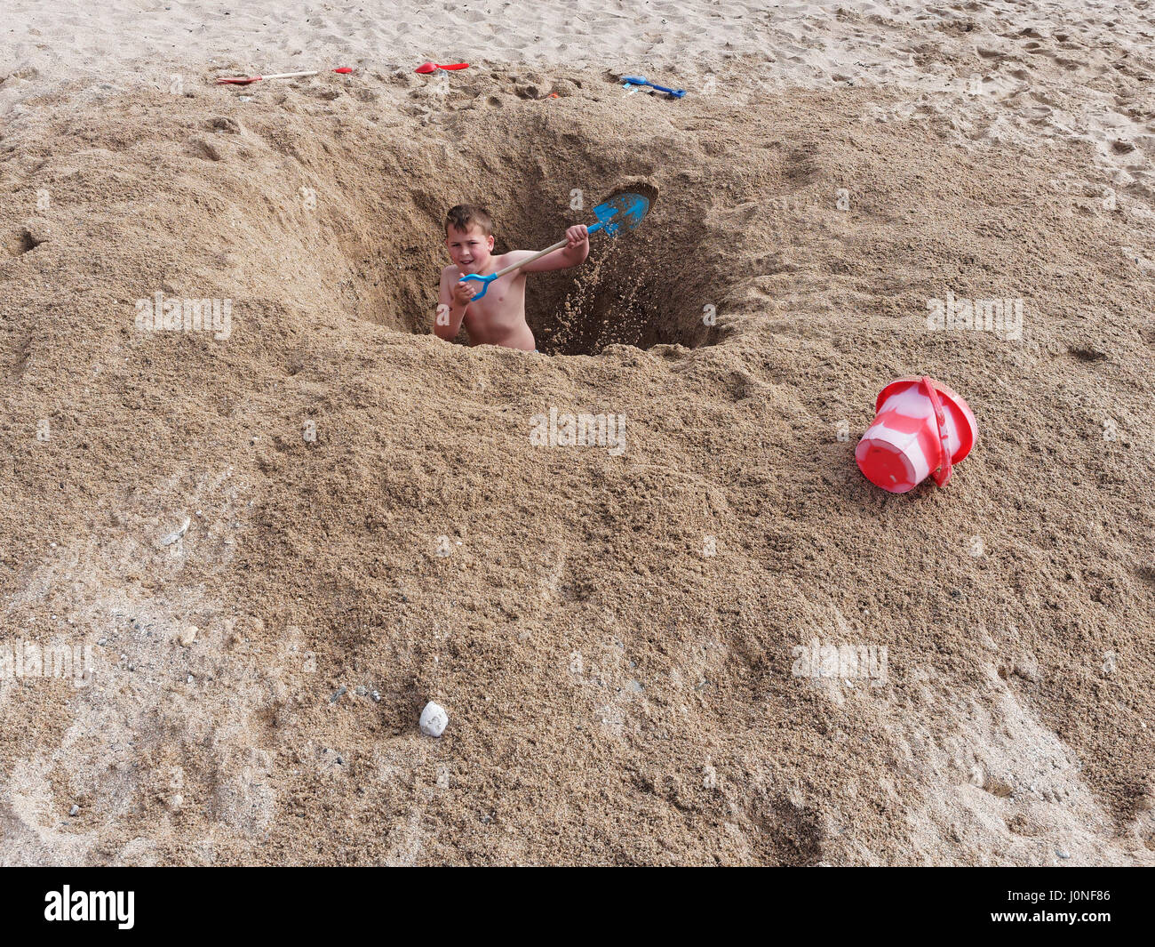 Young boy digs huge hole with bucket and spade on UKbeach Stock Photo