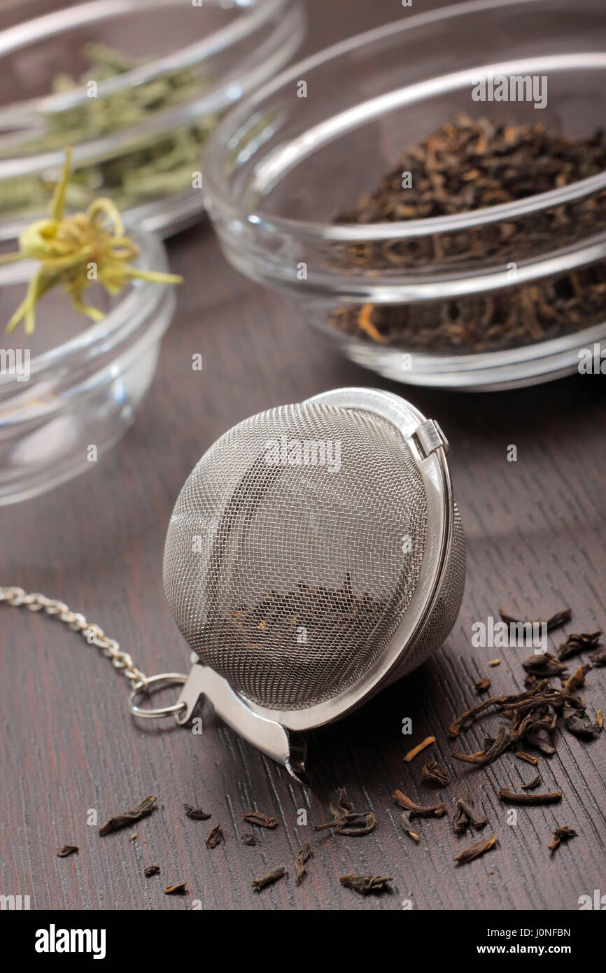 Tea infuser with black tea dried leaves lying on dark board with