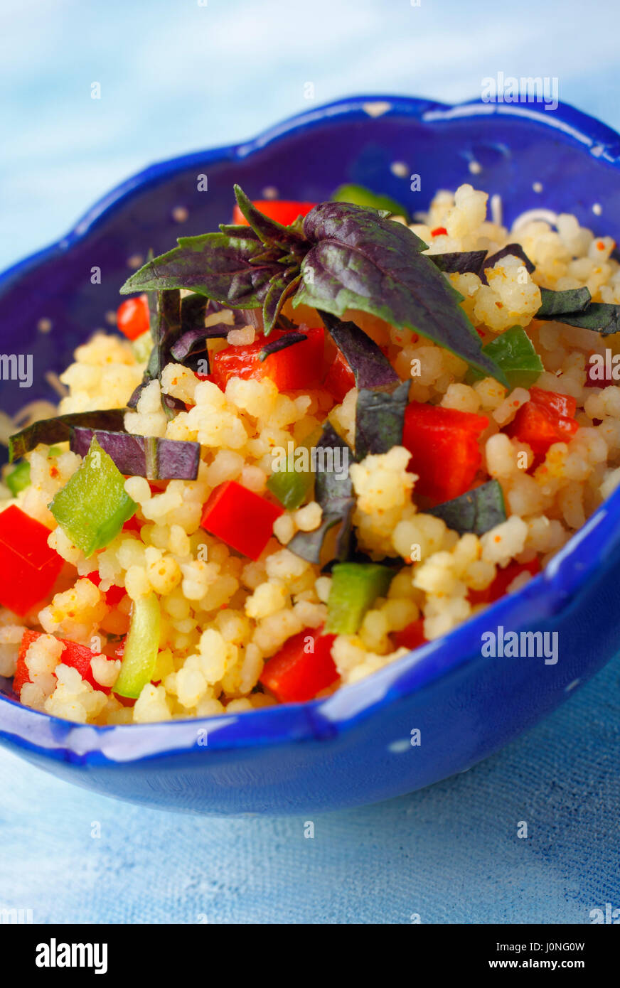 Bowl with couscous, chopped peppers and red basil. Oblique photo. Stock Photo