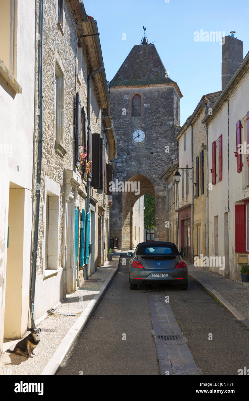 13th Century medieval gateway clock tower, VW Beetle car and dog in ancient bastide town of Duras in Aquitaine, France Stock Photo