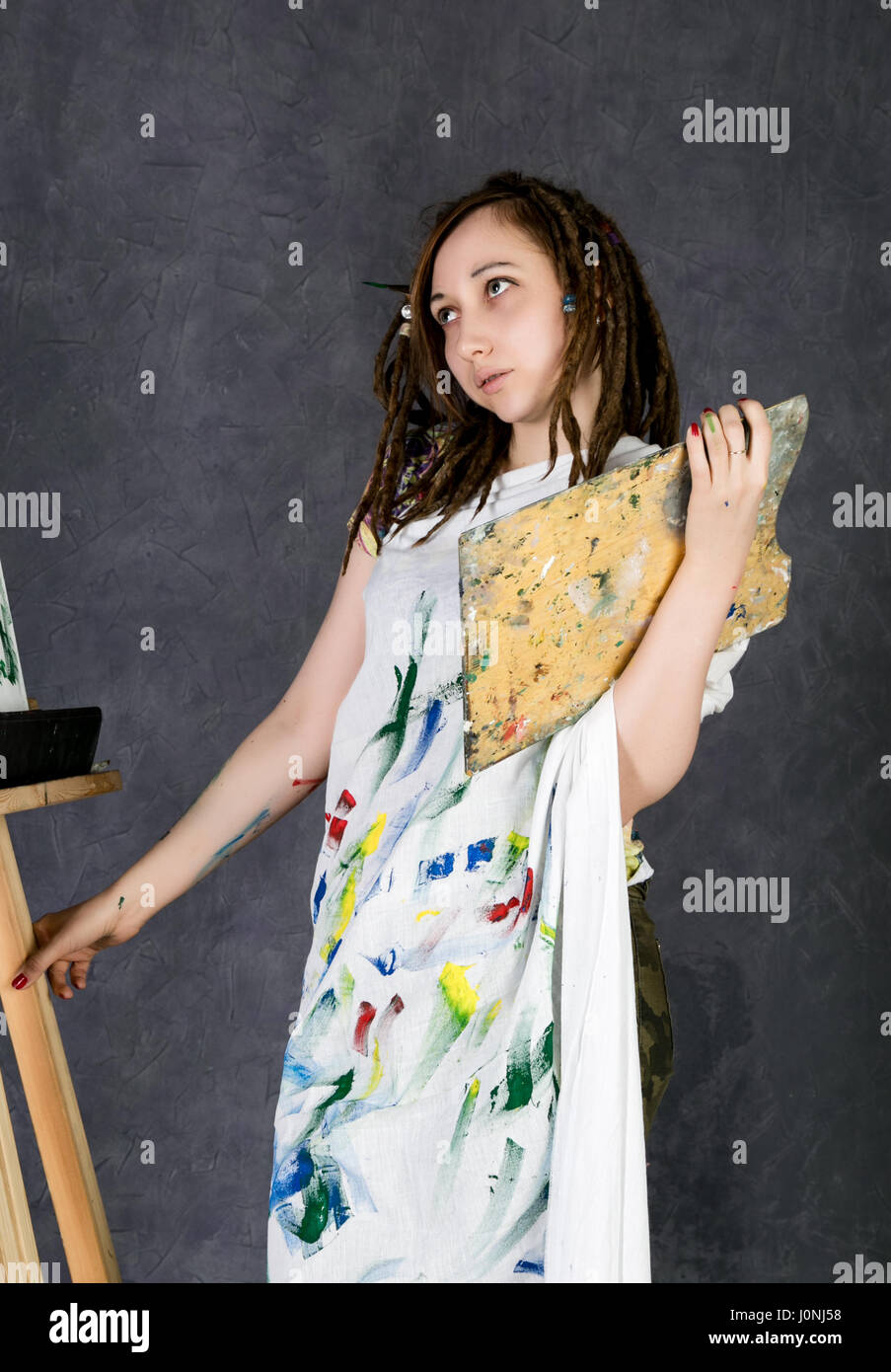 female paint artist posing next to a easel and paints on an canvas ...
