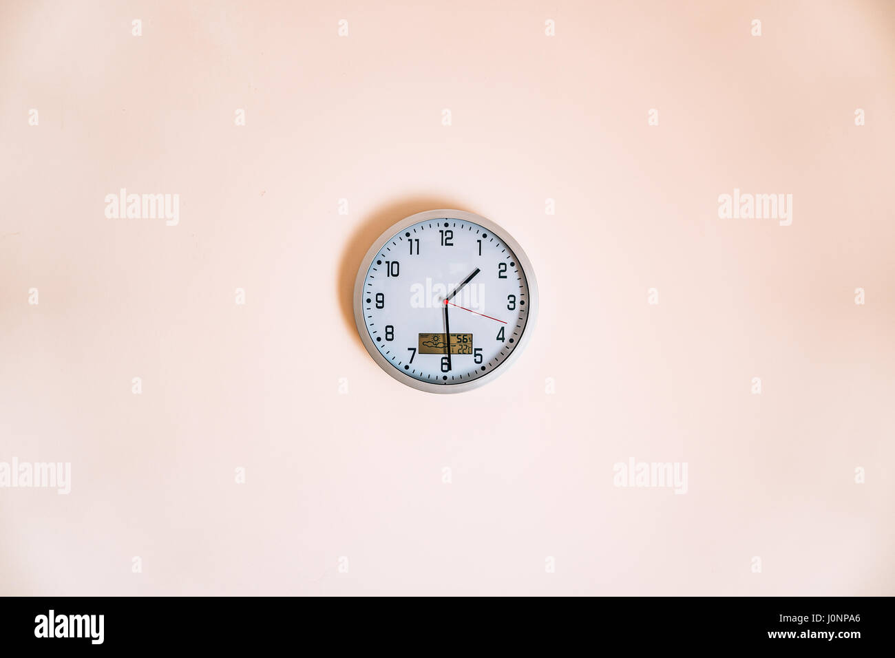 Wall clock in the apartment with a thermometer and weather forecast. Stock Photo