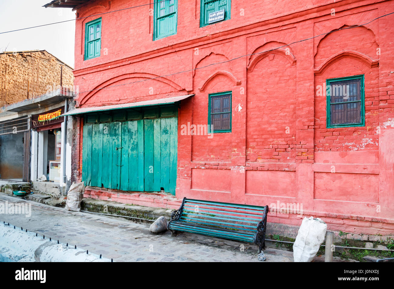 Painted red brick warehouse building with green dilapidated wooden doors, Pragpur, a heritage village in Kagra district, Himachal Pradesh, India Stock Photo