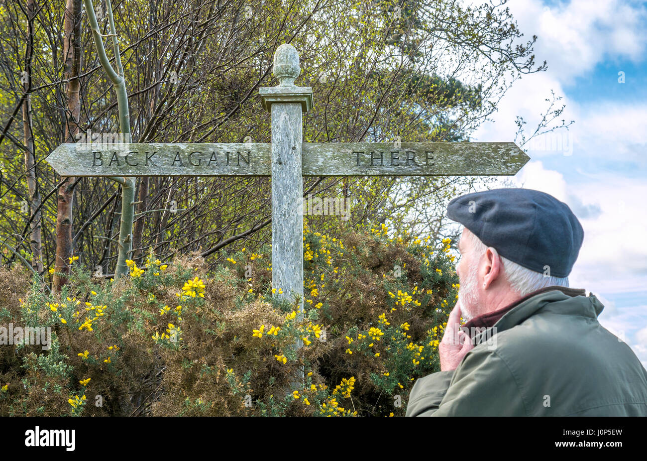 Old man with beard looking puzzled about unusual sign with subtitle There and Back Again, subtitle of The Hobbit by JRR Tolkien, Scotland, UK Stock Photo