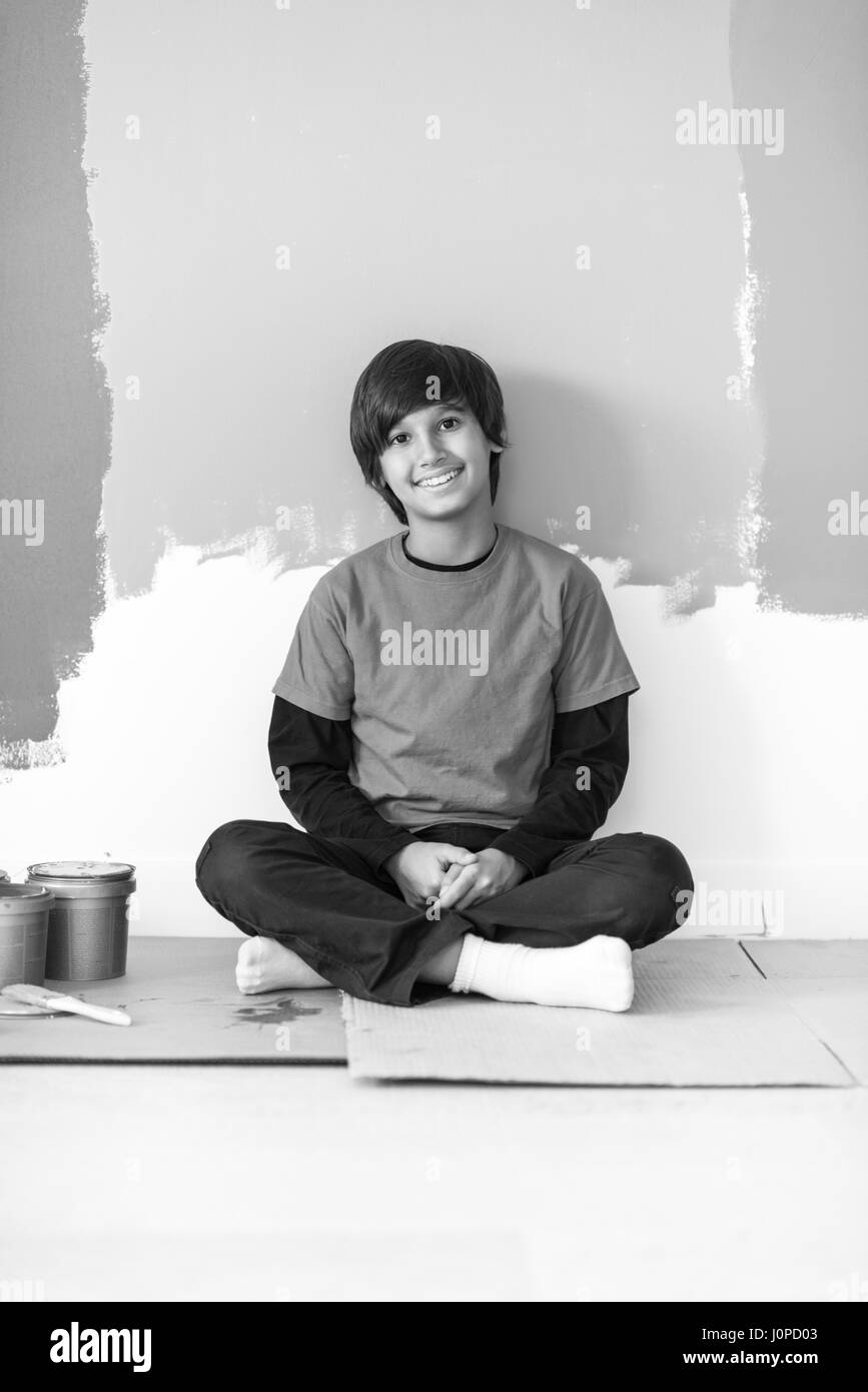 young boy painter resting after painting the wall, sitting on the floor