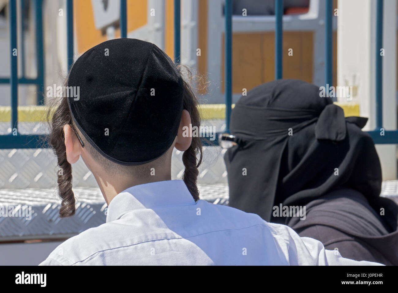 An orthodox religious Jewish boy standing next to a Muslim woman in a hijab at Luna Park in Coney Island, Brooklyn, New York City Stock Photo