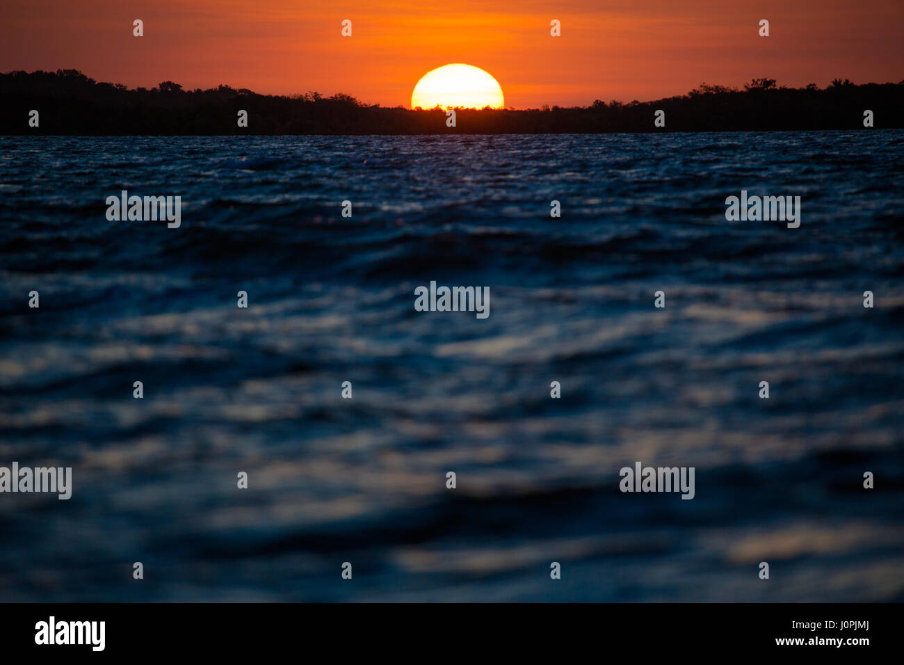 The last moments of sun as it touches an island in silhouette in the Gulf of Carpentaria, Weipa, North Queensland, Australia Stock Photo