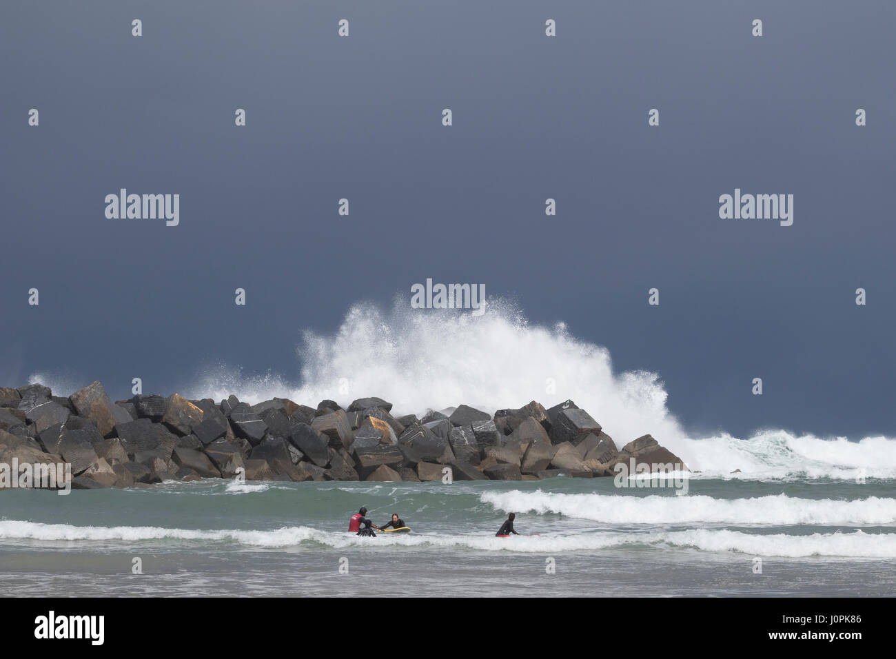 Some surfers protected from big waves by breakwater blocks in La Zurriola beach (San Sebastian, Spain) 2017. Stock Photo