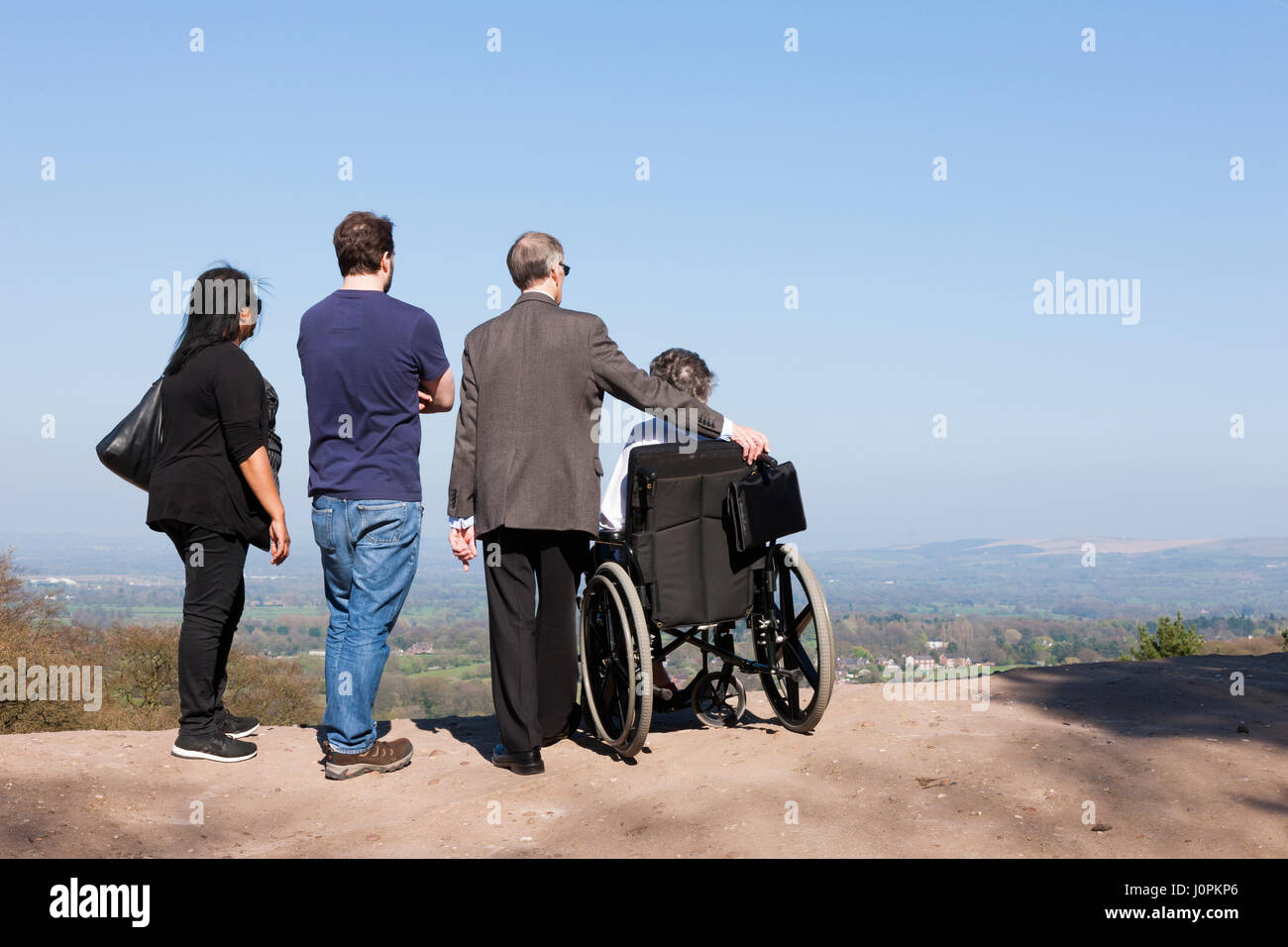 Family sightseeing with one person in a wheelchair enjoy the view / scene / scenery over Cheshire Plain / Plains during day out at Alderley Edge, UK. Stock Photo