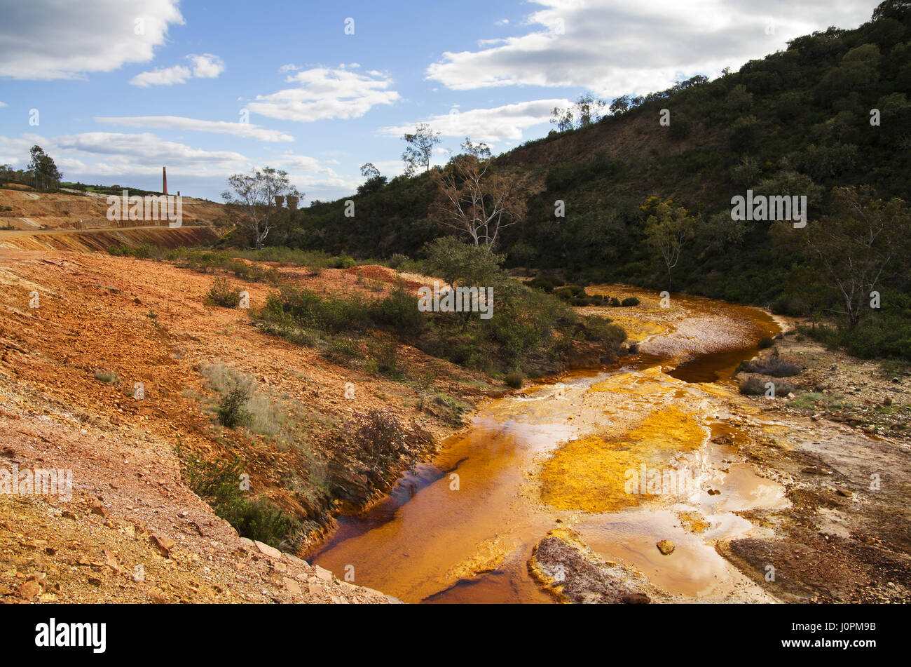 Yellow and red sulfur and iron polluted river bend at Sao Domingos abandoned mine under a blue clouded sky. Mertola, Alentejo, Portugal. Stock Photo
