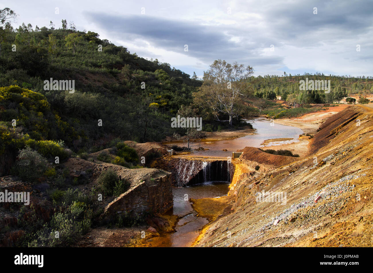 Yellow and red sulfur and iron polluted river going through a dam at Sao Domingos abandoned mine. Mertola, Alentejo, Portugal. Stock Photo