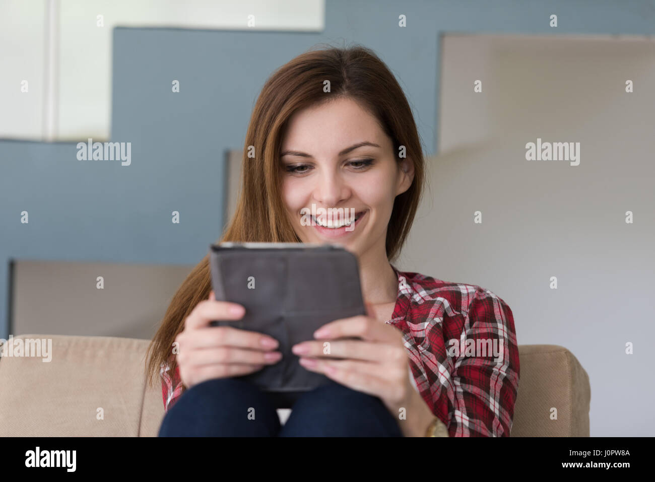 young happy woman sitting on sofa with tablet computer at luxury home ...