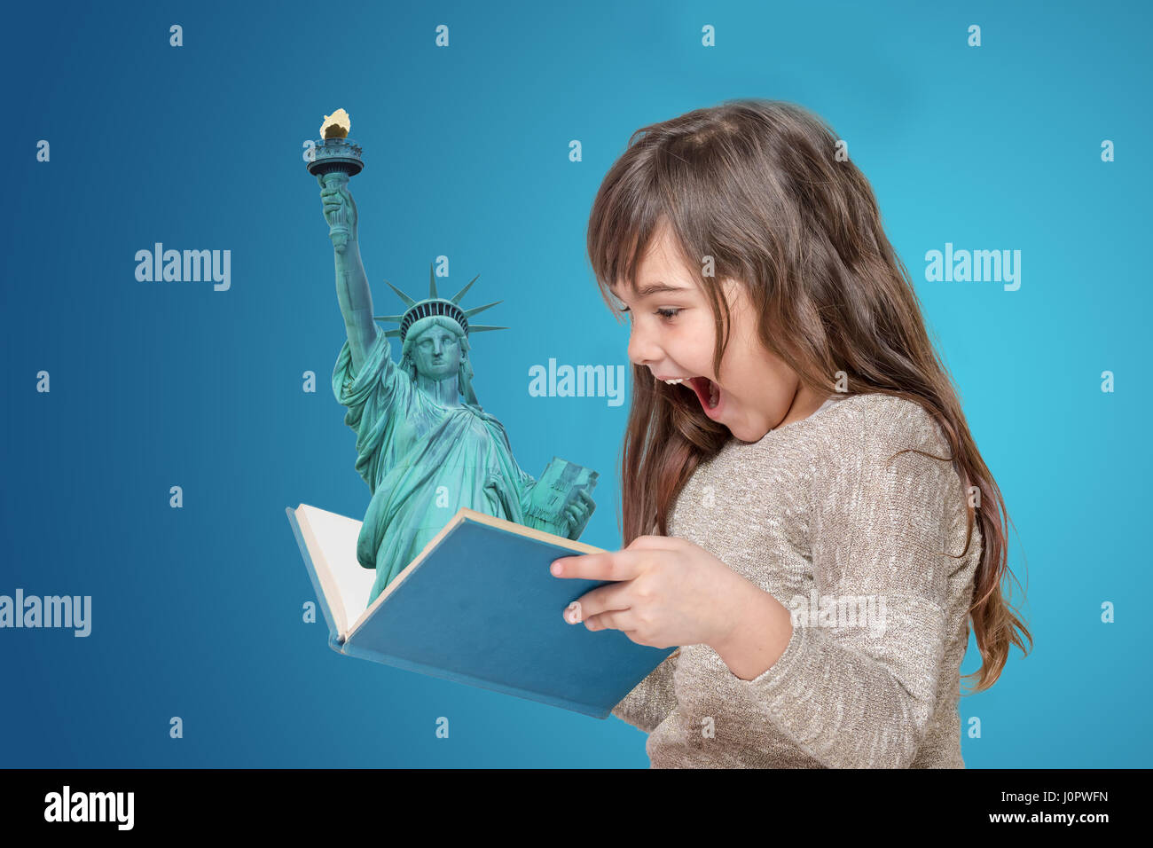 Surprised long haired little girl holding open book in her hands. From the book is protruding Statue of Liberty. All is on the blue gradient backgroun Stock Photo