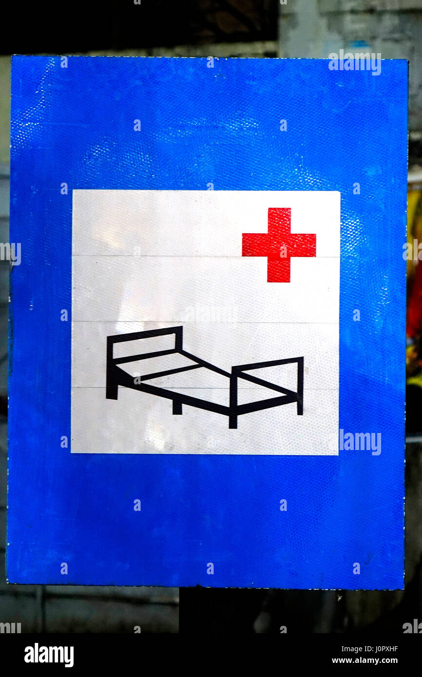 A hospital sign board in street having a hospital bed and red cross sign in white and blue board Stock Photo