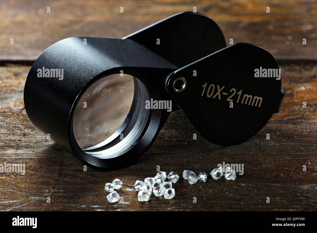 rough diamonds with folding magnifier on wooden background Stock Photo