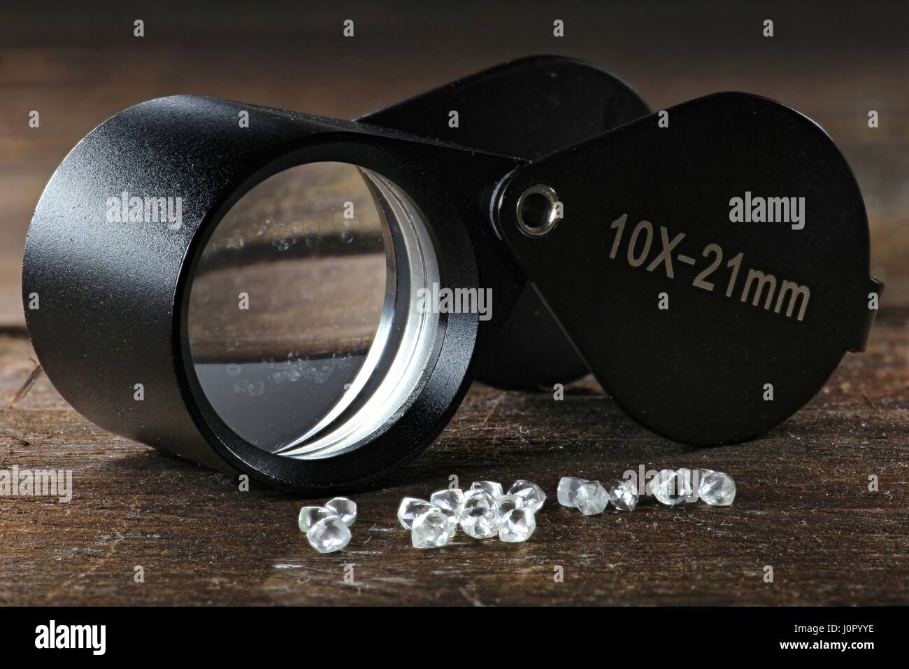 rough diamonds with folding magnifier on wooden background Stock Photo