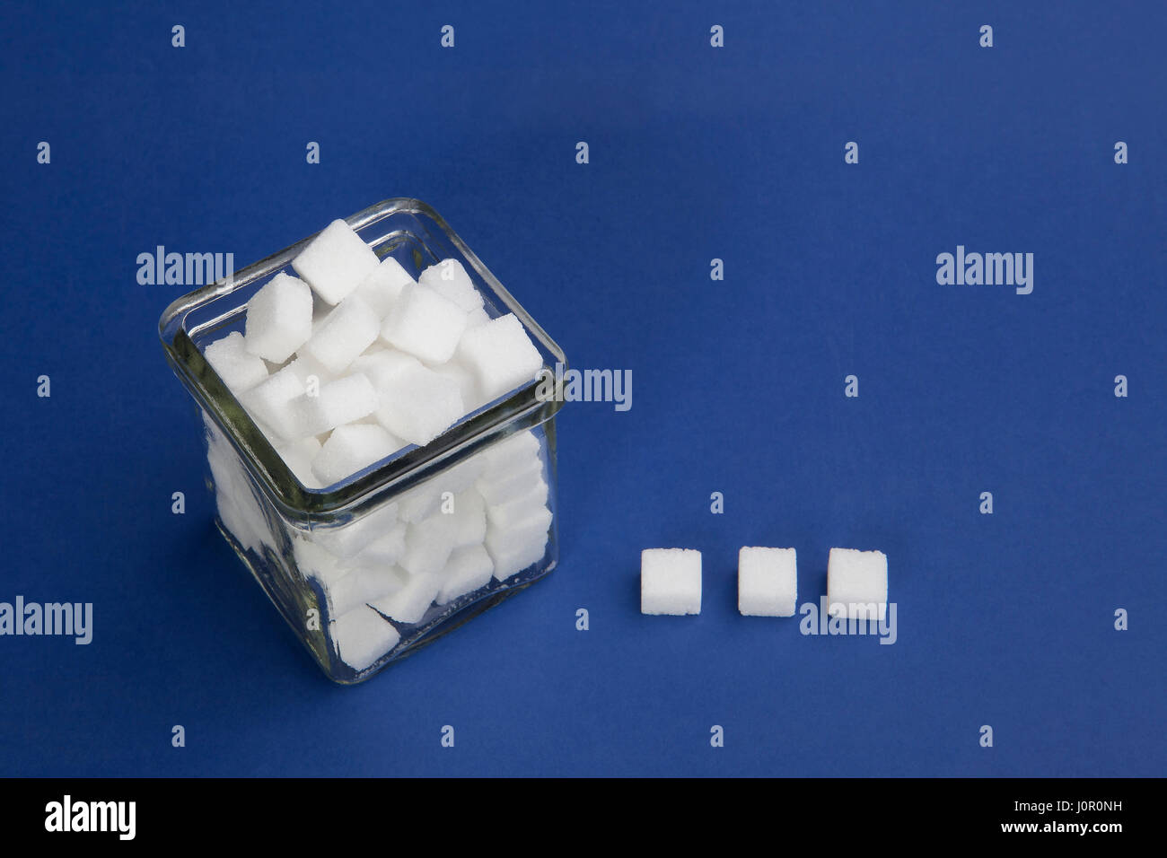 White sugar cubes in a glass bowl on the blue background Stock Photo