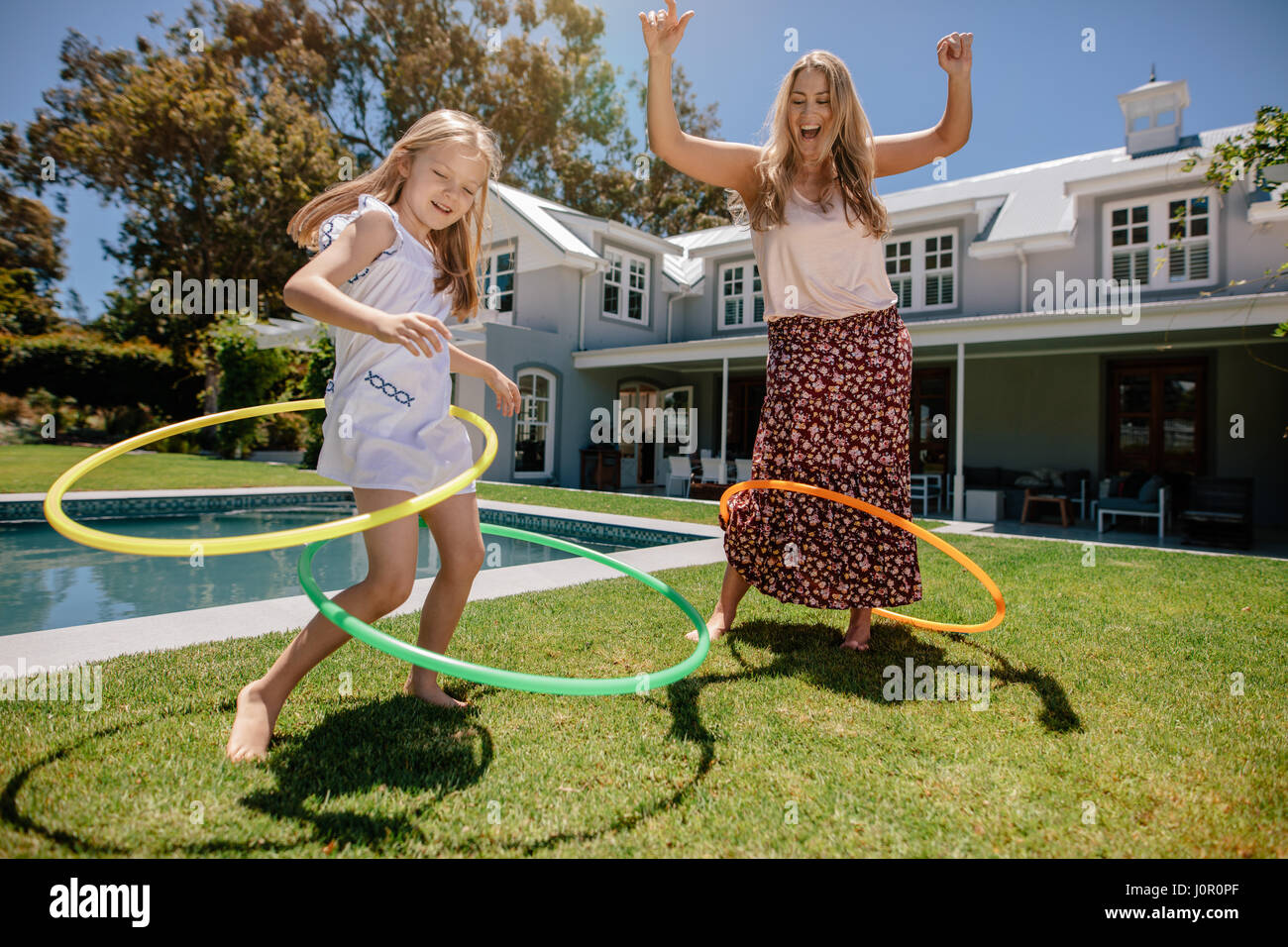 Woman and young girl outdoors using hula hoops and smiling. Mother and daughter playing with hula hoop in their backyard Stock Photo