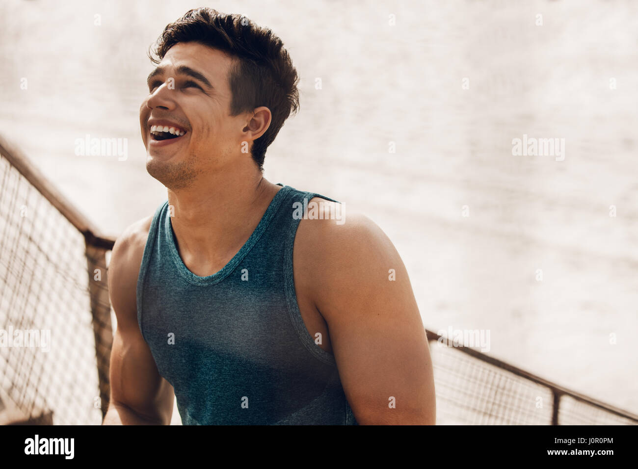 Close up shot of happy young man with muscular body taking a break after workout outdoors. Fit male runner resting after training session at the beach Stock Photo