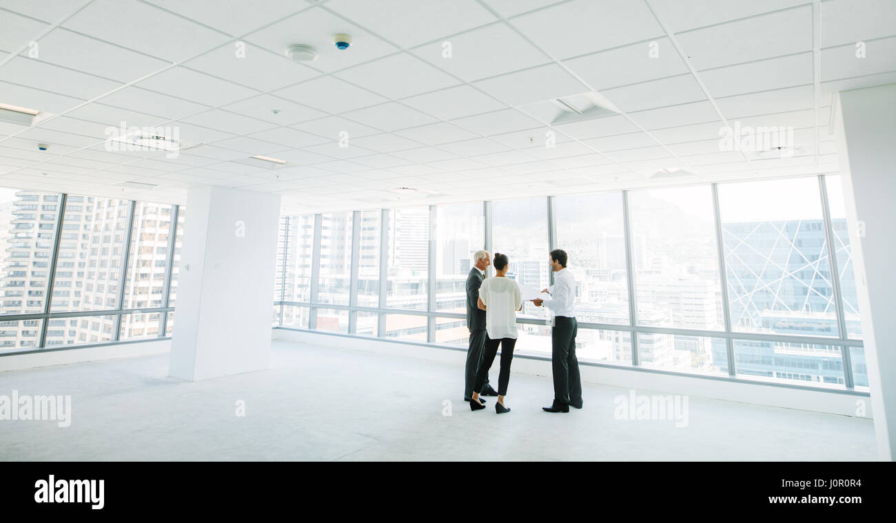 Wide angle shot of real estate agent with potential clients inside an empty office space. Estate broker showing new office space to business people. Stock Photo