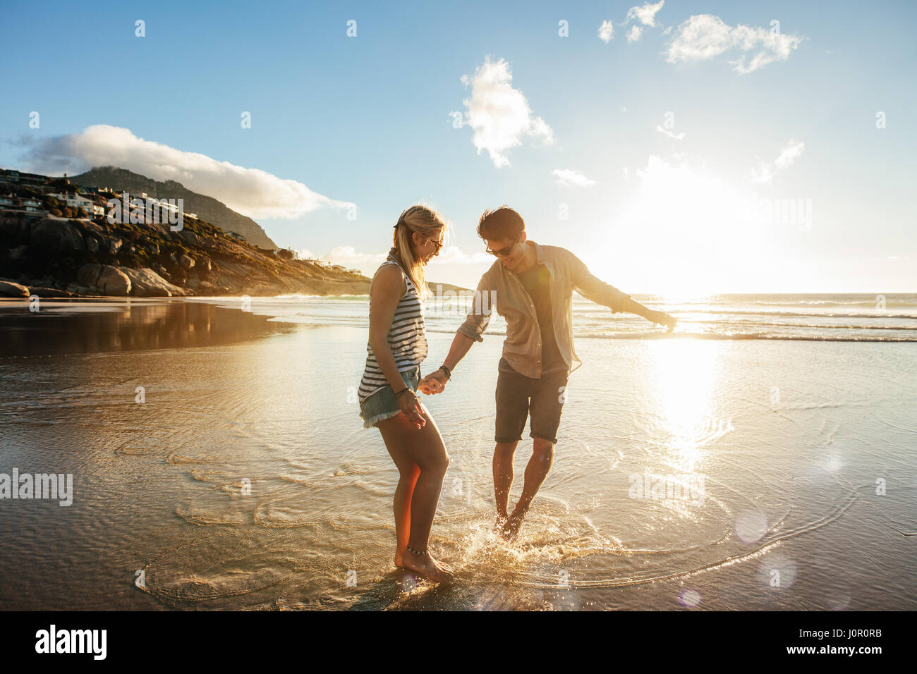 Beautiful young couple holding hands and enjoying together on the shore. Happy young romantic couple in love having fun on beautiful beach. Stock Photo