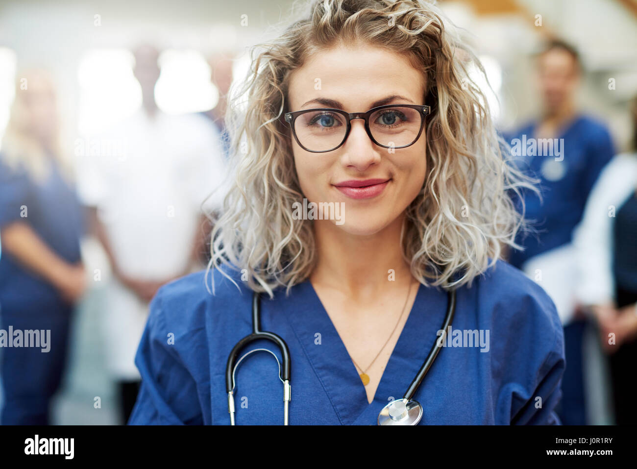 Young female doctor standing in front of medic team at hospital. Female medic smiling to camera Stock Photo
