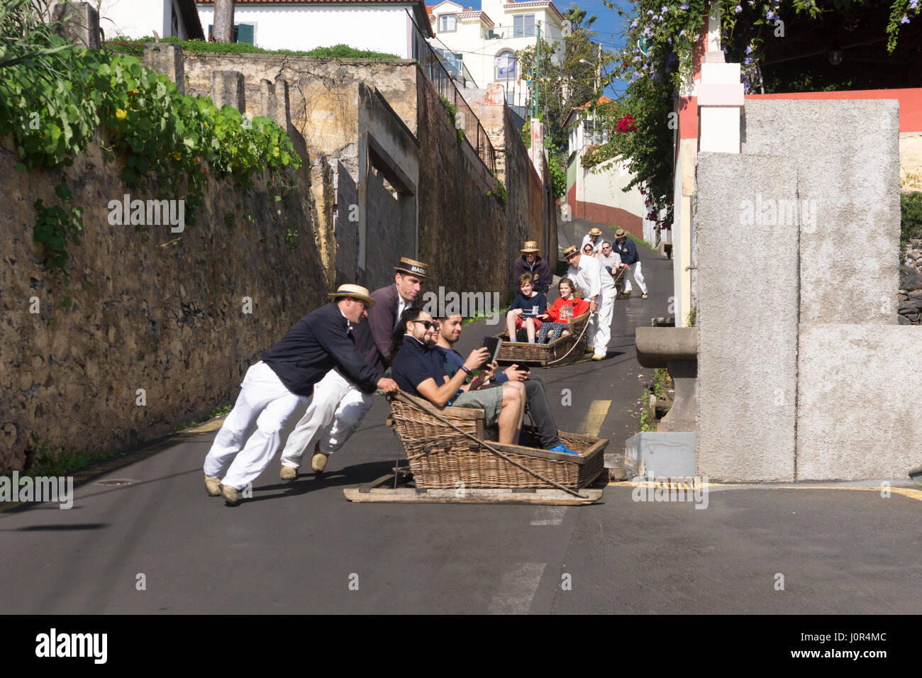 Tourists on the Monte toboggan run, Madeira. Madeira's toboggans are steered by carreiros in wicker boaters on the 2km trip from Monte to Livra-Mento Stock Photo