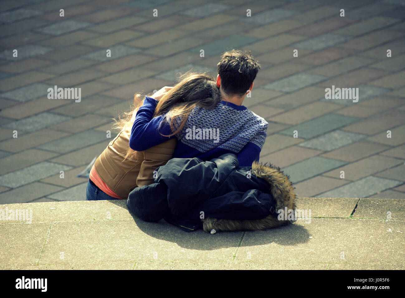 young couple cuddling together boy girl sitting down on the Glasgow concert hall steps at the junction of Buchanan street and Sauchiehall Street Stock Photo