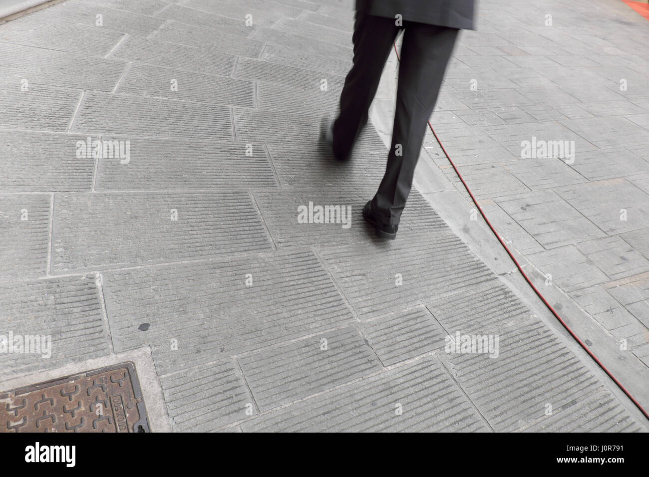 Businessman in grey suit and elegant dark shoes walking in the street (legs and feet only on the sidewalk) - Grey life city street series Stock Photo