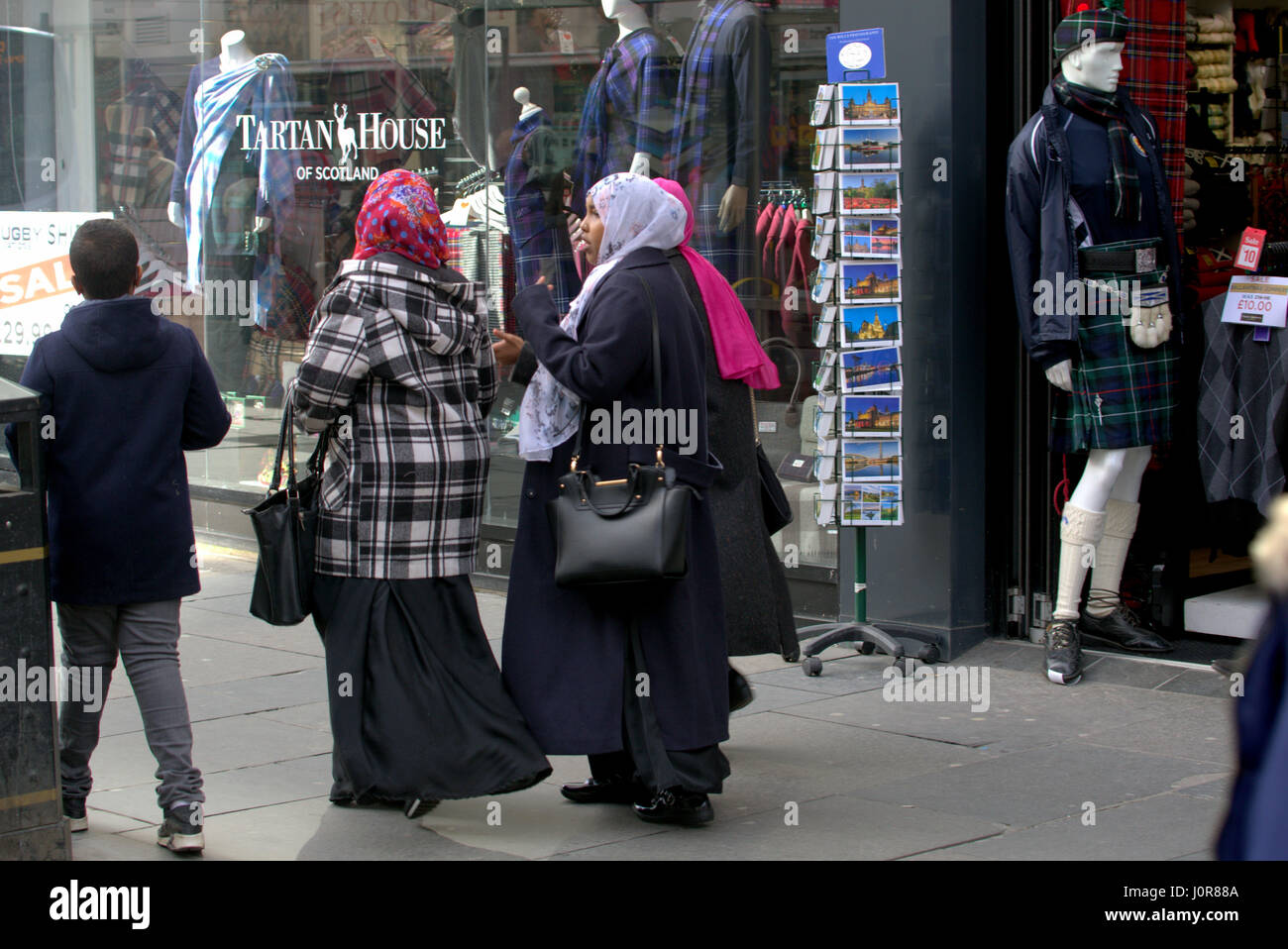 Asian African refugee dressed Hijab scarf on street in the UK everyday scene family walking in crowd with Scottish tartan memorabilia atound Stock Photo
