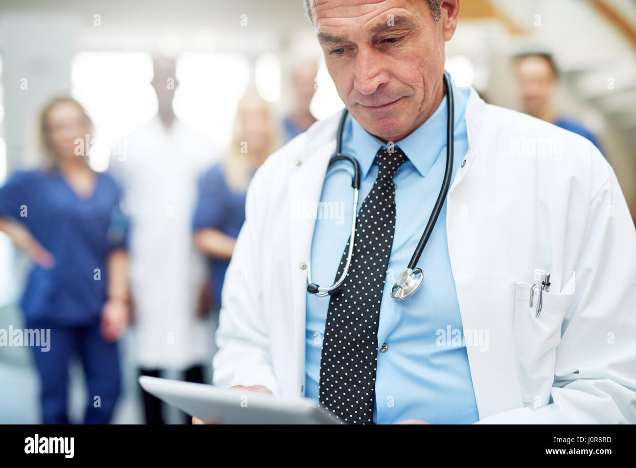 A mature medical professional with stethoscope in the clinic holding the tablet. Stock Photo