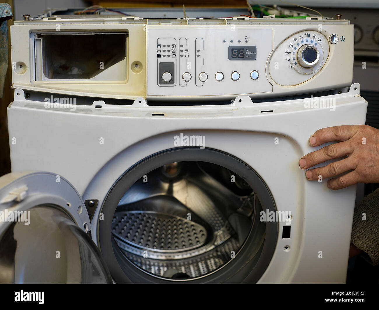 Service man hand holding a front panel of broken washing machine, closeup front shot Stock Photo