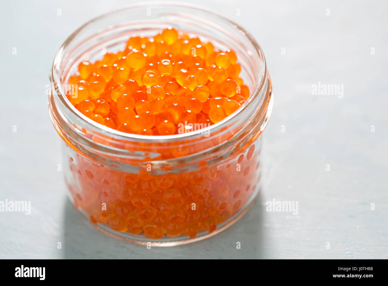 Trout caviar in jar on blue background Stock Photo