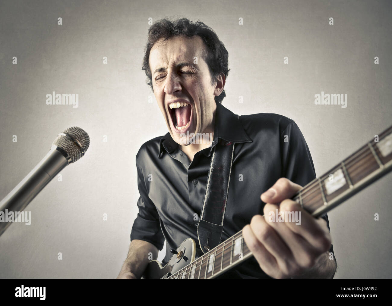Man singing in microphone while playing on guitar Stock Photo