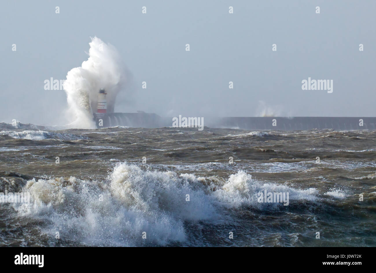 Newhaven Lighthouse in East Sussex, in windy weather with waves breaking over lighthouse, light barely visible. Stock Photo